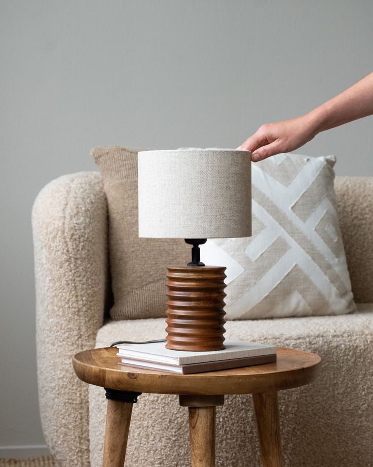 a table lamp sitting on top of a wooden table next to a white pillow and chair