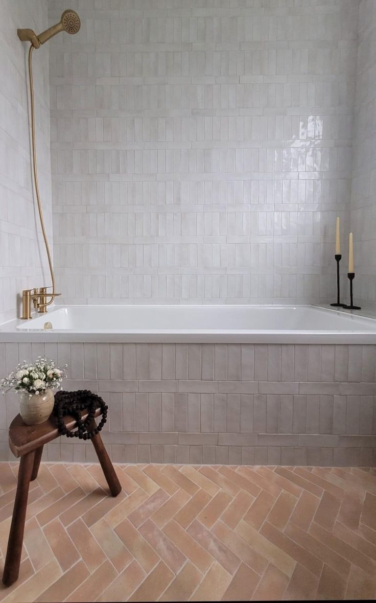 a bath tub sitting next to a wooden bench with flowers on top of it in a bathroom