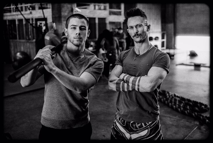 two men standing next to each other in a gym holding baseball bats and looking at the camera