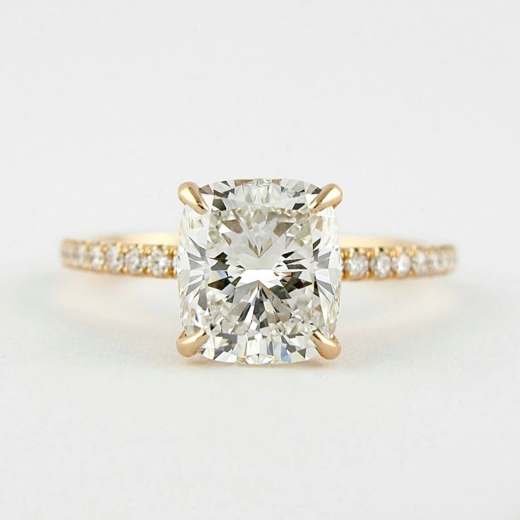 an engagement ring with a cushion cut diamond in the center and pave band around it