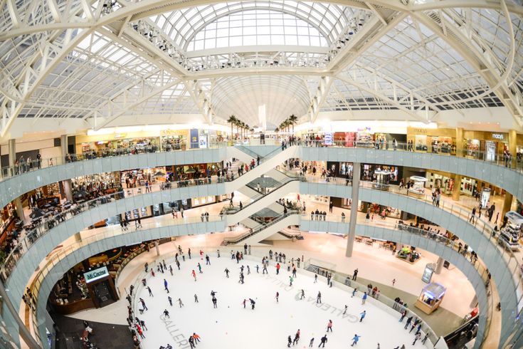 an indoor ice rink with people skating on it and lots of windows above the floor