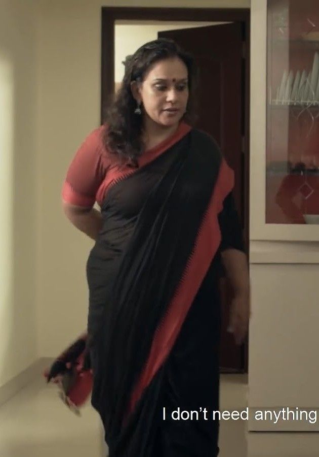 a woman wearing a black and red sari standing in front of a door with the words i don't need anything written on it