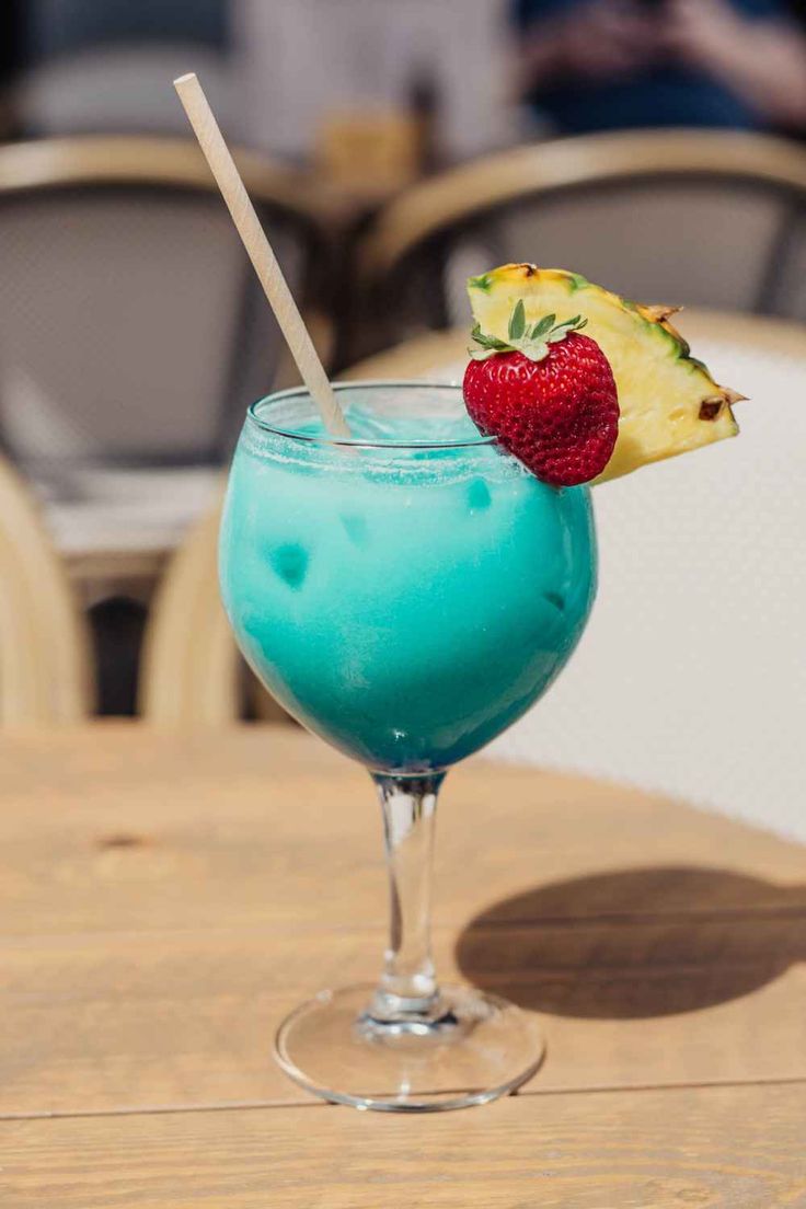 a blue drink sitting on top of a table next to a strawberries and pineapple