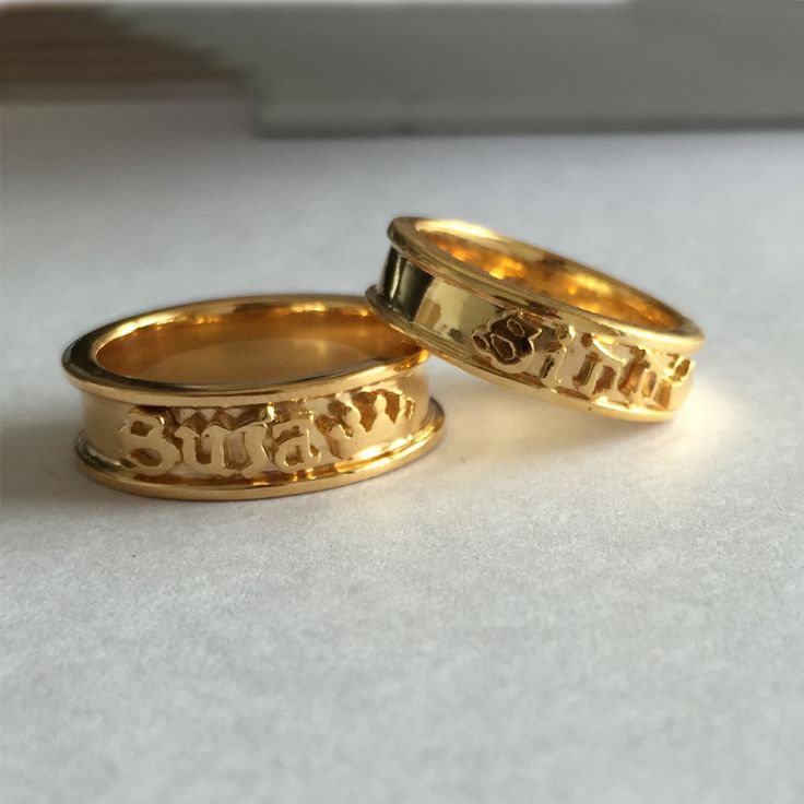 two gold wedding rings with the word love written on them, sitting next to each other