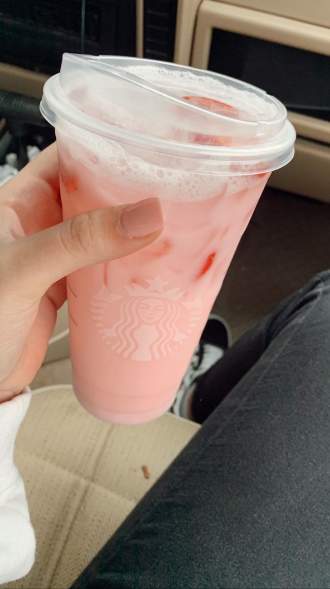 a person holding up a pink drink in the back seat of a car with their thumb on it