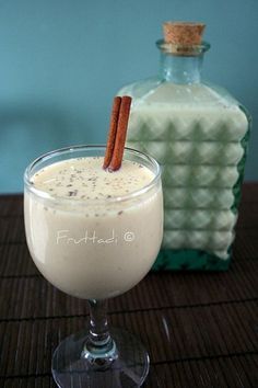 a drink in a glass with cinnamon sticks sticking out of it and a bottle next to it