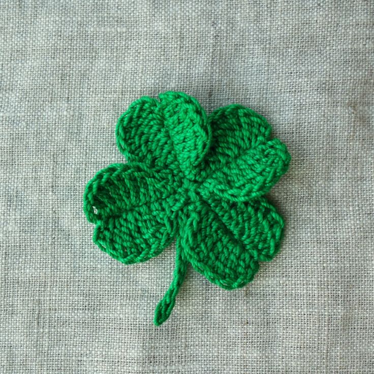 a green crocheted clover sitting on top of a gray cloth