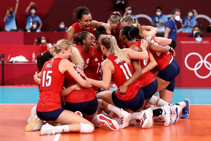 a group of women's volleyball players huddle together on the court