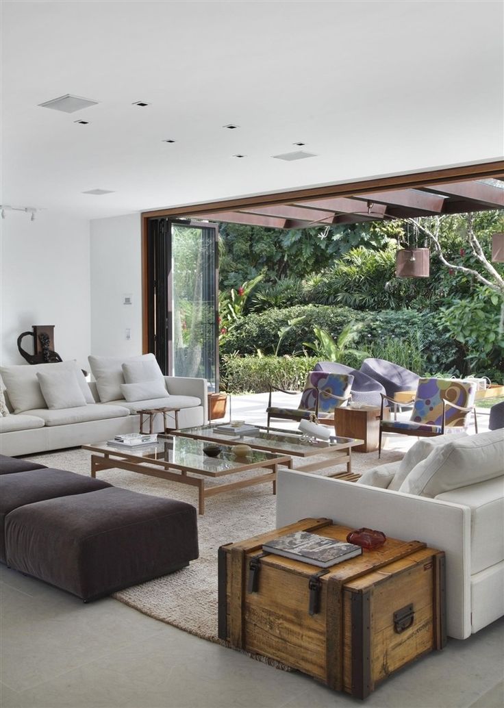 a living room filled with white furniture and lots of glass doors leading to a lush green forest