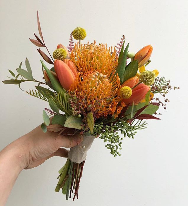 a hand holding a bouquet of flowers on a white background with greenery and leaves