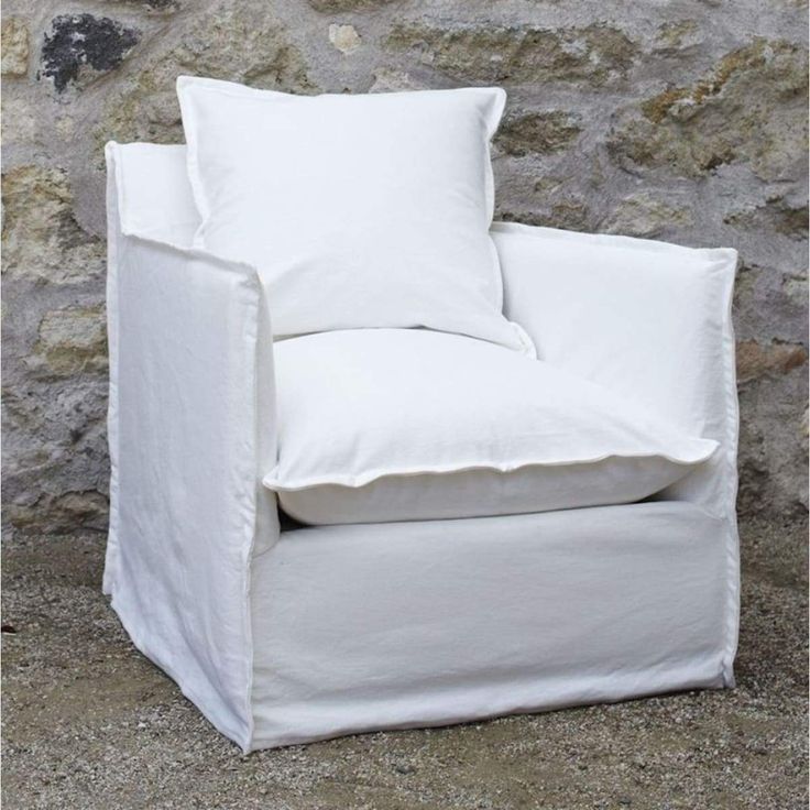 a white chair sitting next to a stone wall with two pillows on top of it