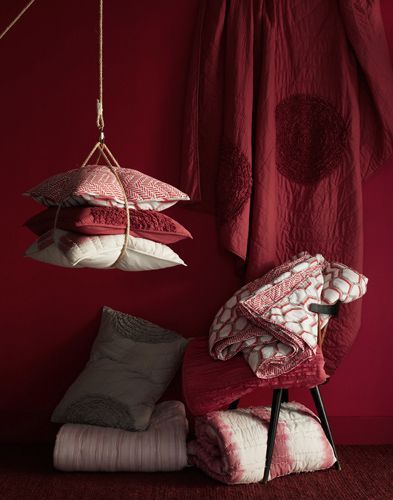 a red chair and some pillows in front of a red wall with hanging lights on it