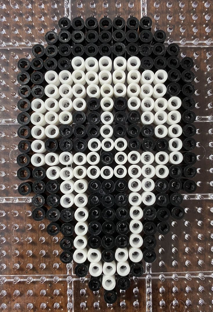 a skull made out of black and white plastic beads on a wooden surface with the word's symbol