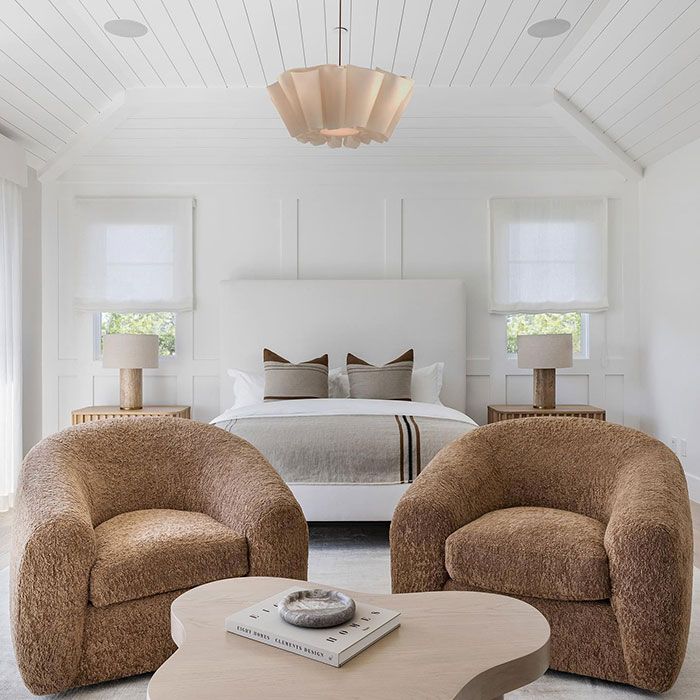 two chairs and a coffee table in a room with white walls, carpeted flooring and large bed