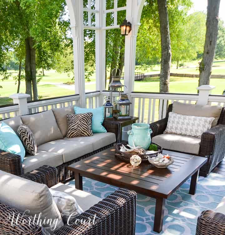 an outdoor living room with wicker furniture and blue rugs on the porch area