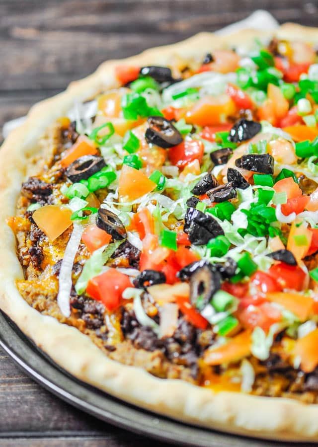 a pizza topped with lots of toppings sitting on top of a metal pan next to a wooden table