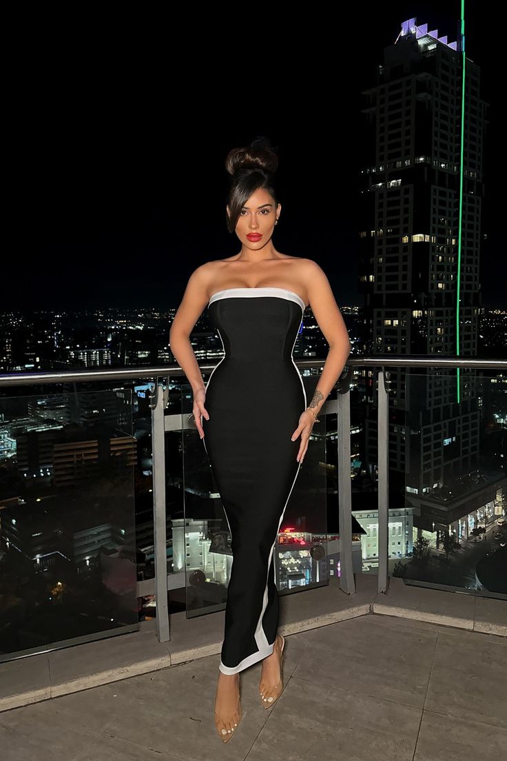 a woman in a black and white dress standing on top of a building at night