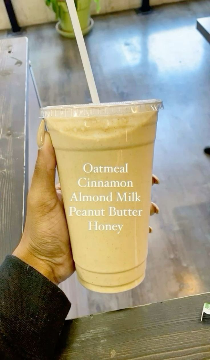 a person holding up a cup with a straw in it that says oatmeal cinnamon almond milk peanut butter honey