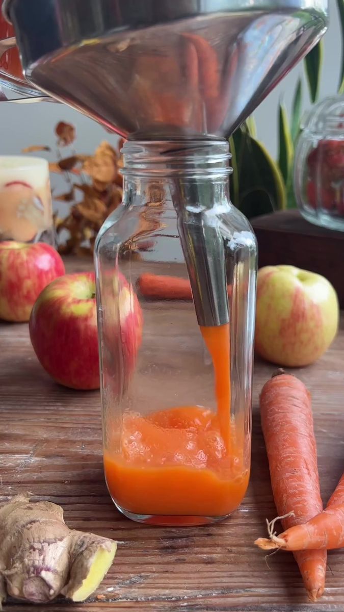 carrot juice being poured into a mason jar with an apple and ginger in the background