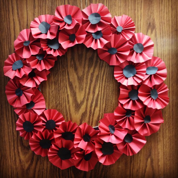 a wreath made out of red paper on top of a wooden table next to a wall