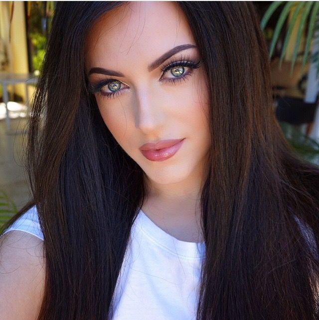 a woman with long black hair and blue eyes is posing for a photo in front of a palm tree