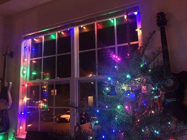 a christmas tree is lit up in front of a window with colorful lights on it