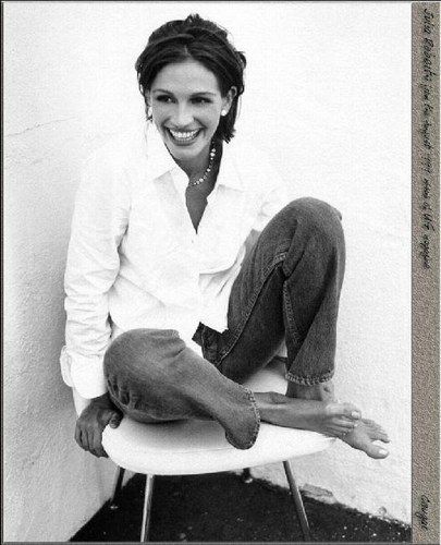 a black and white photo of a woman sitting on a chair smiling at the camera