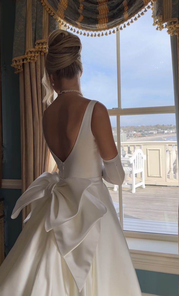 a woman in a white wedding dress looking out the window with her back to the camera