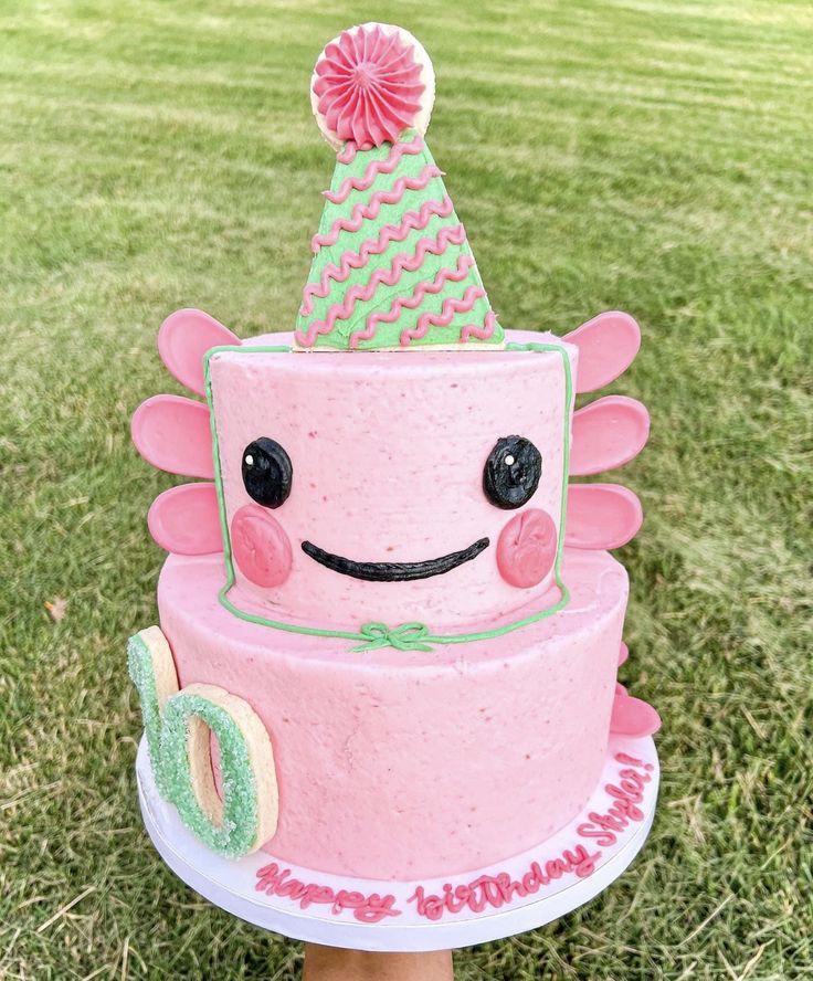 a pink birthday cake sitting on top of a lush green field