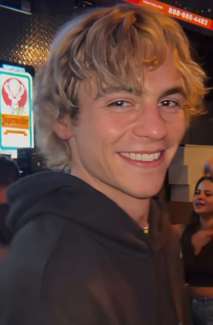 a young man with blonde hair smiles at the camera while standing in front of a group of people