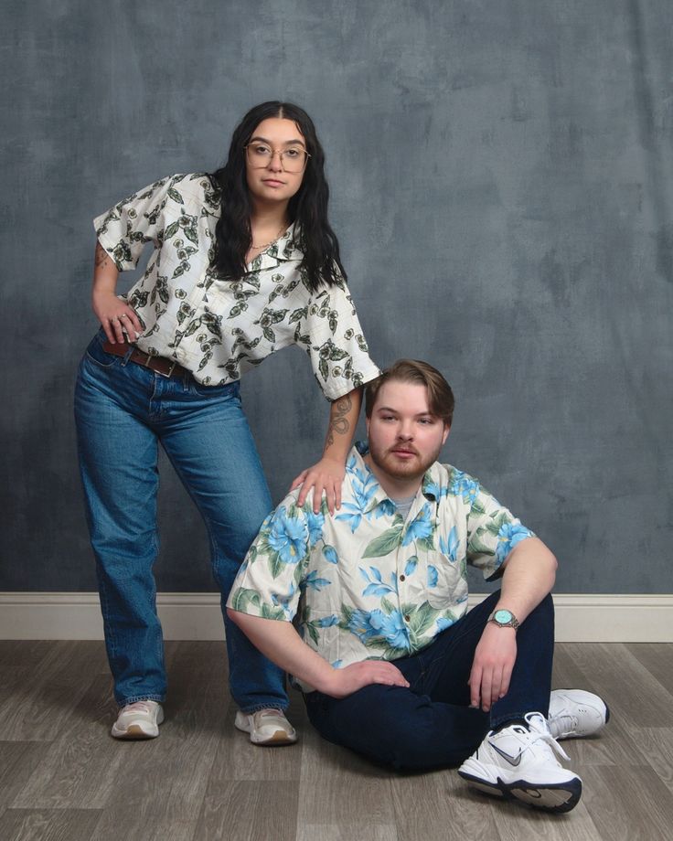 a man sitting on the floor next to a woman in front of a gray wall