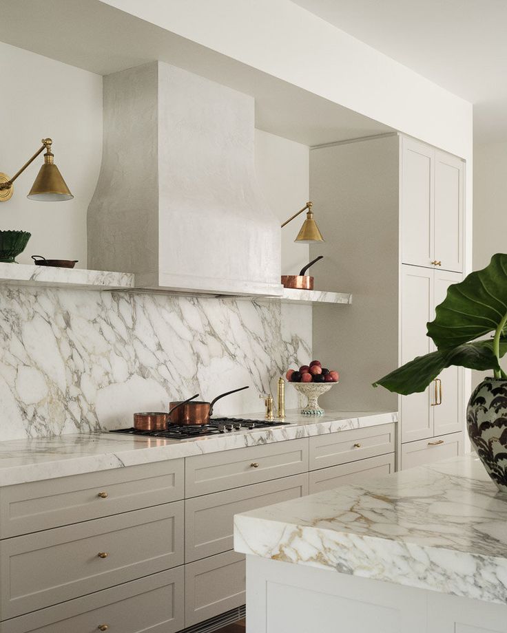 a kitchen with marble counter tops and gold accents on the hood, along with white cabinets