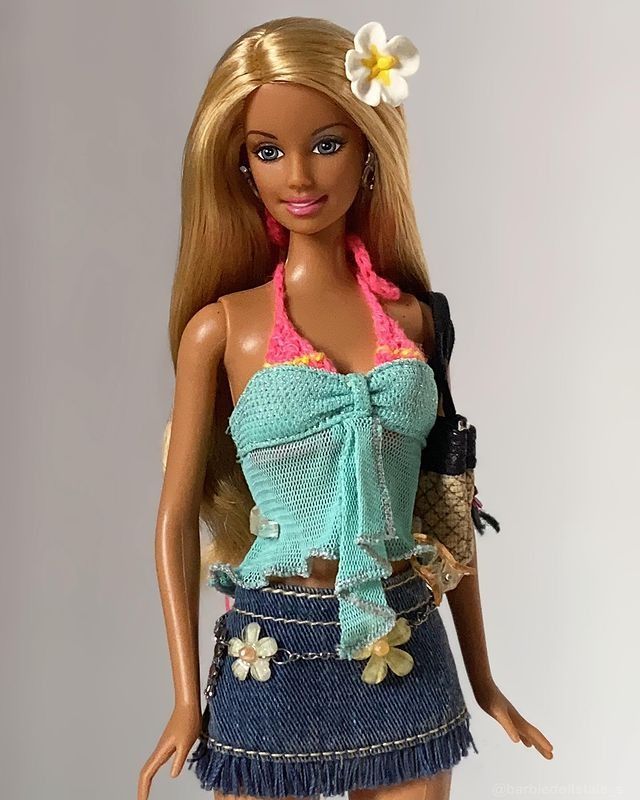 a barbie doll wearing a blue skirt and pink top with flowers in her hair, holding a purse