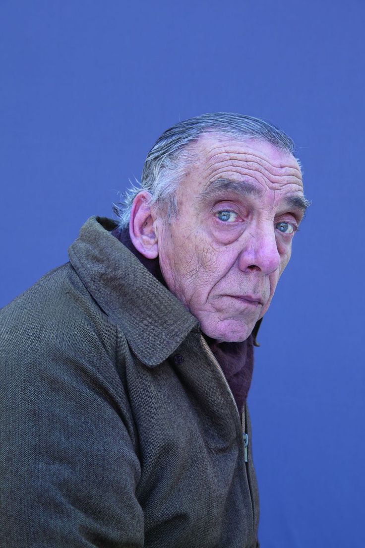 an old man is looking at the camera while wearing a brown coat and jacket with his hands on his hips