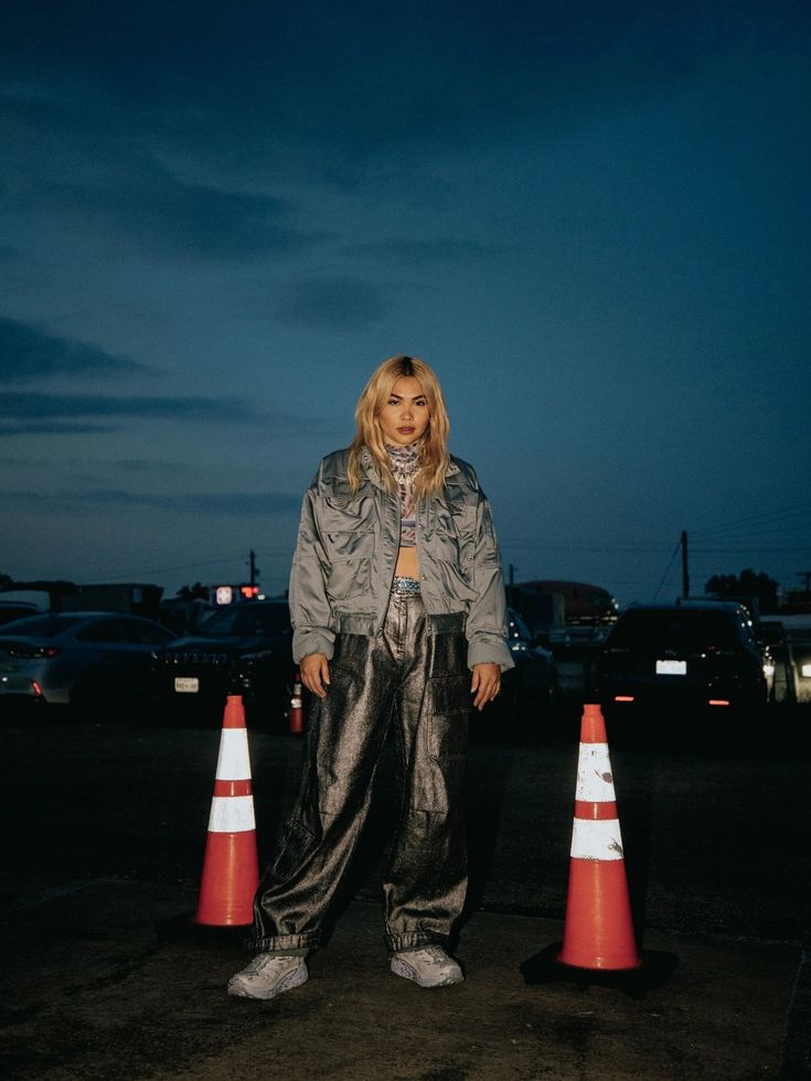 a woman standing in front of traffic cones at night with her hands on her hips