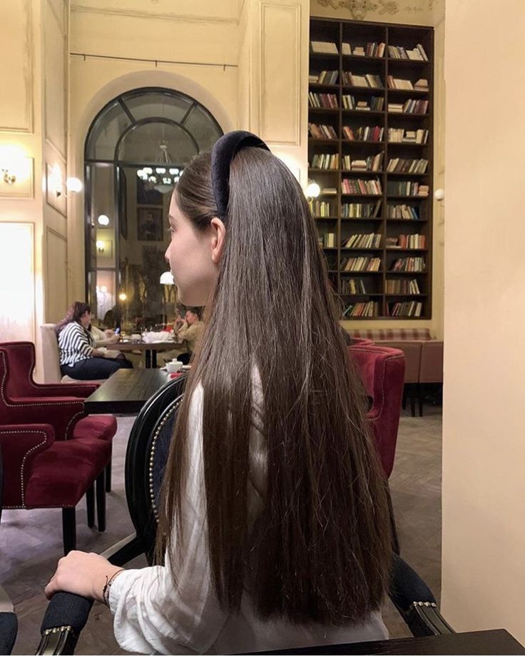 a woman with long hair sitting in front of a book shelf filled with lots of books