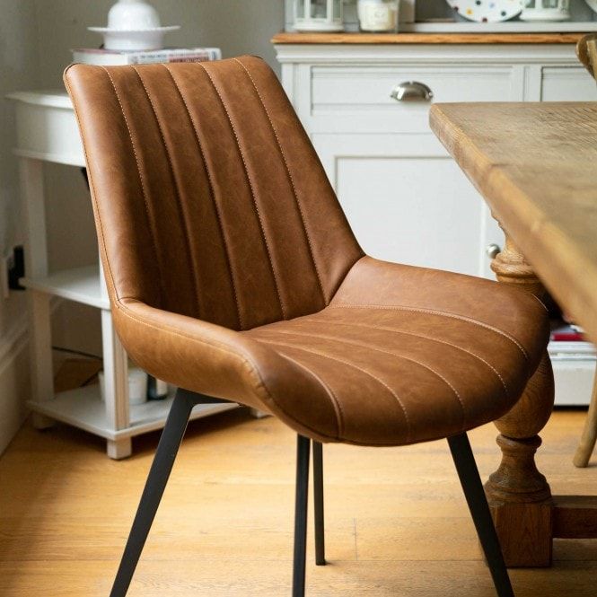 a brown leather chair sitting in front of a wooden dining room table and white cabinets