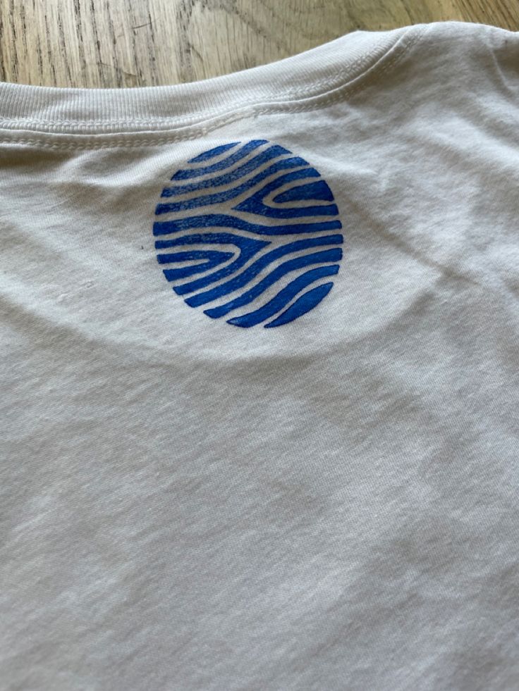 a white t - shirt with a blue circle on it sitting on top of a wooden table