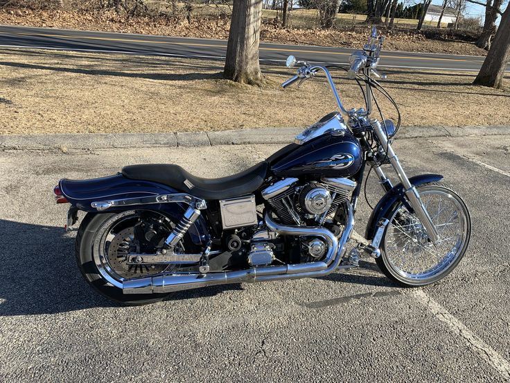 a black motorcycle parked in a parking lot next to some trees and grass with no leaves on it