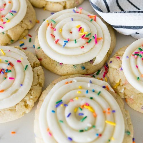 cookies with white frosting and sprinkles are on a plate next to a towel