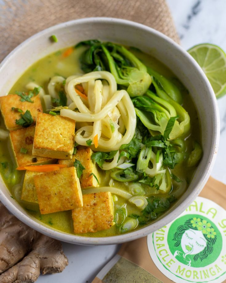 a bowl of soup with tofu, broccoli and noodles on the side