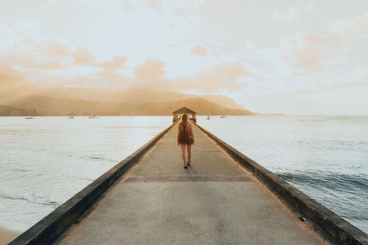 a woman walking down a pier towards the ocean