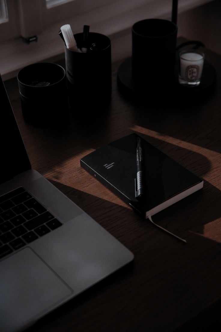 an open laptop computer sitting on top of a wooden desk next to a cup and pen