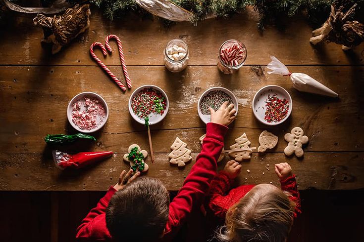 two children making christmas cookies on a wooden table with candy canes and candies