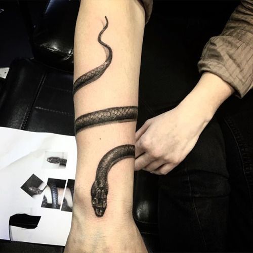 a person with a tattoo on their arm holding onto a black and white snake wrist