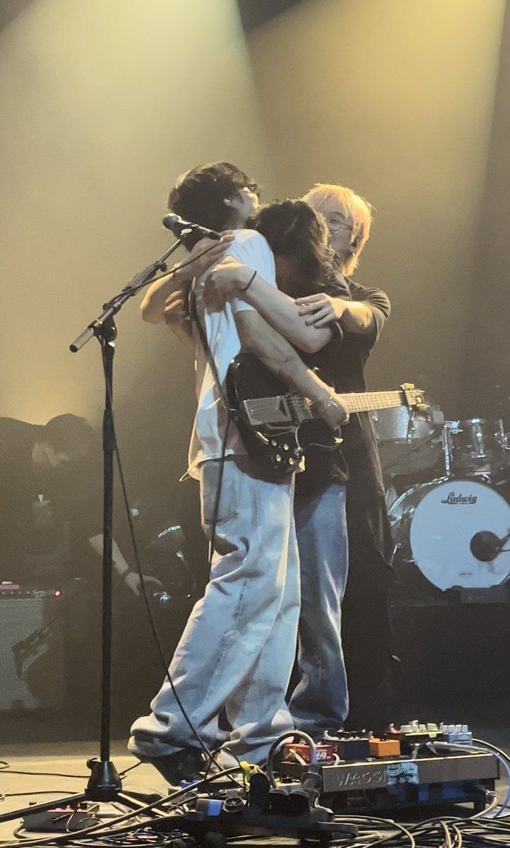 two men hugging each other while standing on stage with microphones in front of them