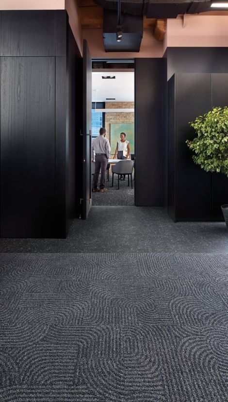 two people are sitting at a table in an office with black walls and carpeted floors