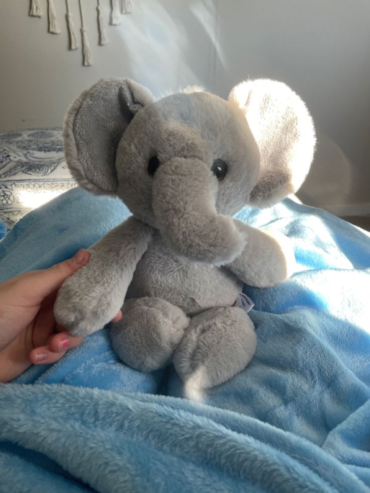 an elephant stuffed animal sitting on top of a blue bed sheet in someone's hand