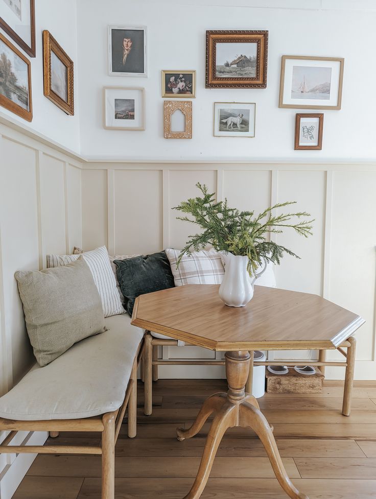 a wooden table sitting next to a white bench in a room with pictures on the wall