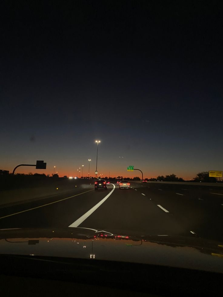 cars driving down the highway at night with street lights in the distance and traffic signs on either side